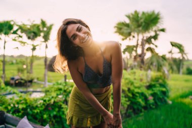 Güneşli yerleri ziyaret eden neşeli kadın turistin yarım boy portresi, kameraya gülümseyen komik kız yaz tatili boyunca samimi bir şekilde gülüyor.