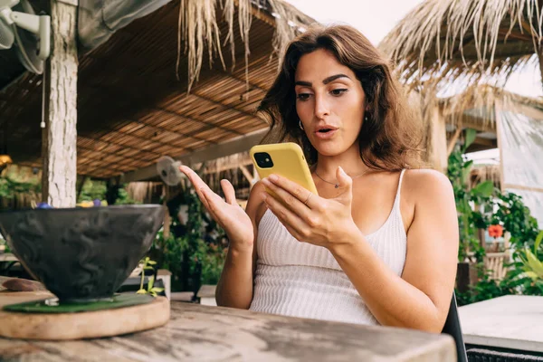 熱帯の国の屋外カフェテリアで食べ物のボウルとテーブルに座っている間 驚きの少数民族の女性のサーフィン携帯電話の低角度 — ストック写真