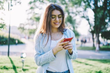 Göz giysili neşeli hippi kız, akıllı telefon çalma listesine şarkı indiriyor bahar gününü parkta geçiriyor, radyo uygulamasına bağlanan gülümseyen bir kadın, boş zamanlarında cep telefonu ve kulaklık kullanıyor.