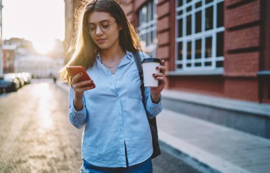 Gözlüklü, vizyon koruması için beyaz kadın cep telefonuyla mesaj okuyor, sokakta boş zaman geçiriyor, kahve servisi yapan genç hippi kız blogunda akıllı telefon kullanıyor.