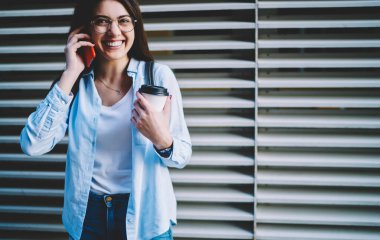 Optik gözlüklü neşeli beyaz kadın kahve molası sırasında akıllı telefondan aradığı için gülüyor. Cep telefonuyla konuşan komik bayan turist internet bağlantısını kullanarak cep telefonuyla konuşuyor.