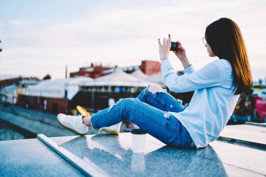 Gündelik giysiler giymiş genç bir kadının modern akıllı telefondan fotoğraf çekerken arka plan görüntüsü. Hücresel uygulamayla video bloğu etkileyen yenilikçi kız 4G kablosuz bağlantı kullanıyor.