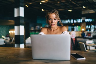Çağdaş kreatif kafeteryadaki akıllı telefonuyla tezgahta otururken netbook üzerinde çalışan sakin genç bayan