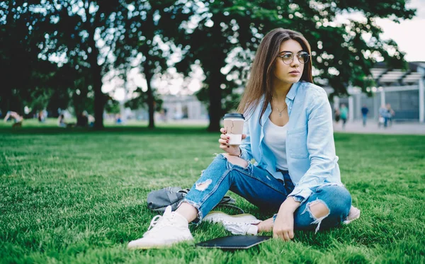沉思的女学生 带着外卖的咖啡因饮料 躺在公园的草地上 戴着光学眼镜沉思的白人妇女 在春天的时候为保护视力沉思 — 图库照片