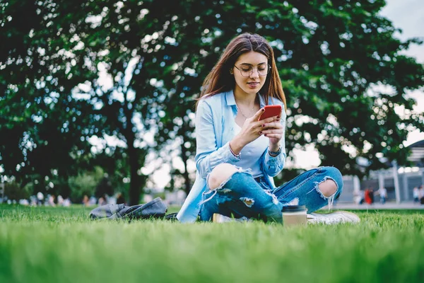 公園で4Gワイヤレスに接続するオンラインメッセージングのための携帯電話のガジェットを使用して古典的なアイウェアで白人ヒップスターの女の子 スマートフォンアプリをインストールしながら 若い女性ブロガーネットワーキングソーシャルメディア — ストック写真