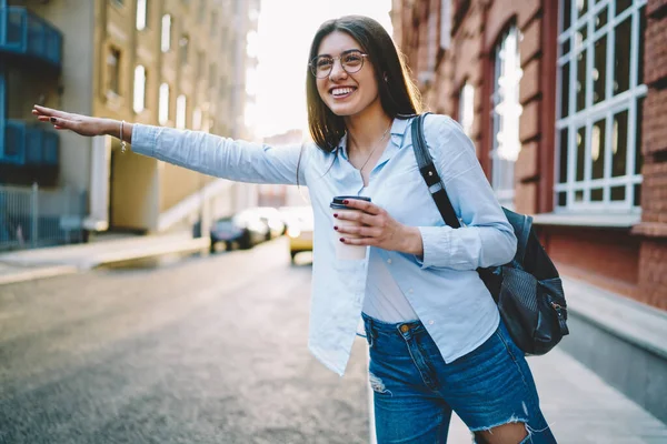 快乐快乐的女人 戴着眼镜 站在路边保护视力 准备停车 有趣的白人嬉皮士女孩 拿着咖啡 一边坐公交一边笑 — 图库照片