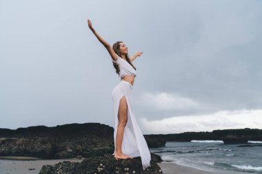 Vücudunun tamamından memnun bir kadın kollarını kaldırarak özgürlüğün tadını çıkarırken başka tarafa bakıyor ve gülümsüyor.