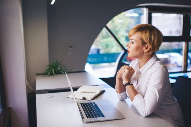 Dizüstü bilgisayarı açık bir şekilde masada oturup düşünürken elleri bağlı kadın çalışanın yan görüntüsü.