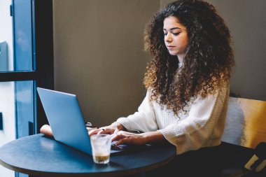 Millennial kadın, internet üzerinden internet üzerinden internet bağlantısı kullanarak internet videosu izliyor, kıvırcık saçlı yetenekli bir serbest yazar, netbook ekranında taranmış.