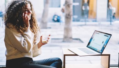 Elinde kafein içeceği olan mutlu kıvırcık serbest yazar cep telefonu aygıtını kullanarak internet projeksiyoncusu, bilgisayarlı neşeli hippi kız ve dost canlısı cep telefonu konuşmasının keyfini çıkarıyor.