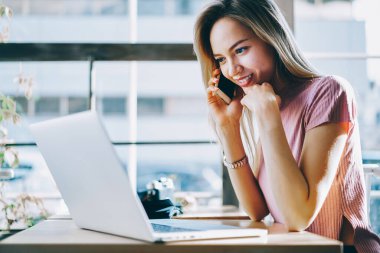 Neşeli metin yazarı 4G internet bağlantısı kullanıyor serbest iş sırasında telefon görüşmesi yapıyor, akıllı telefonla konuşan mutlu bir kadın modern dizüstü bilgisayarda taranmış video yayınını tartışıyor.