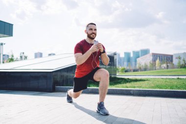 Kulaklıklı iyimser bir erkek sporcu sabahları antrenman yaparken müzik dinliyor ve cep telefonuyla mesajlaşıyor.