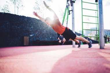 Gün ışığında spor sahasında zaman geçirirken, kollarını uzatarak iple fonksiyonel antrenman yapan kararlı sporcunun yan görüntüsü
