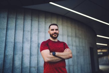 Kaslı sakallı, akıllı erkek antrenör kollarını kavuşturup antrenman sırasında yalnız başına kameraya bakıyor.