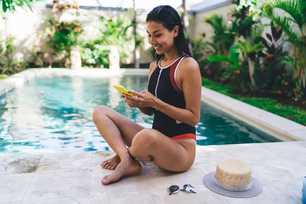 Side View Cheerful Ethnic Female Swimwear Sitting Swimming Pool Texting — Stockfoto