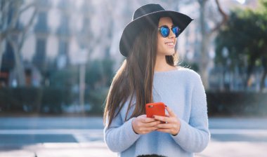 Tatillerde gülümseyen mobil teknolojili modaya uygun giyinmiş kadın blogcu, kaçış yolculuğunun ve akıllı telefon aygıtıyla medya ağı kurmanın keyfini süren mutlu Kafkasyalı turist