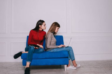 Tam boy konsantre bayan öğrenciler günlük kıyafetleriyle rahat mavi arabada oturuyorlar ve ödevlerini yaparken dizüstü bilgisayar ve notlarla birlikte