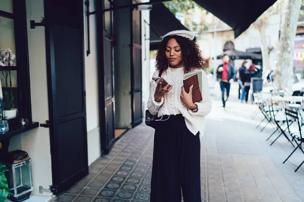 ストリートを歩き スマートフォンを閲覧しながら音楽を聴くカジュアルな服やベレー帽の若いアフリカ系アメリカ人女性のコンテンツ — ストック写真