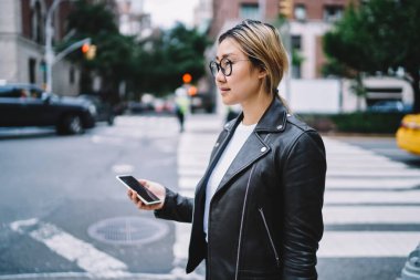 Yeni moda deri ceketli ve görüş düzeltmesi için şık gözlüklü düşünceli bir milenyum kullanıcısı. Tatillerde gezmeyi ve seyahat etmeyi düşünüyor. Modern cep telefonlu Çinli blogcu.