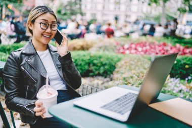 Optik gözlüklü mutlu kadın grafik tasarımcısı uzaktan kumanda sırasında web içeriğini tartışarak uluslararası olumlu bir konuşma yapıyor, dizüstü bilgisayarlı gülümseyen hippi kız