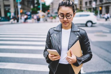 Çevrimiçi rezervasyon ve bankacılık için 4G inetrnet 'e bağlanan optik gözlüklü kadın blog yazarı eskiz defterli Çinli hippi kız şehir sokaklarında akıllı telefon notlarını kontrol ediyor.