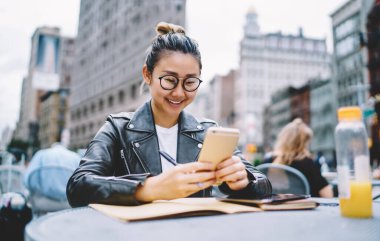 Milenyum kadın blogcu gözlüklü modern cep telefonu teknolojisi ile video bloğu izliyor, sosyal medyada akıllı telefon ağı web sitesi ile gülümseyen hippi kız 4G kablosuz internet kullanıyor