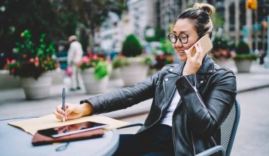 Deri ceketli Japon milenyumu ve vizyon koruması için klasik gözlükler. Arkadaşını buluşmayı planlamak için sokak kafeteryasında dolaşma bağlantısını kullanıyor. Uygulamayla arayan Asyalı kadın.