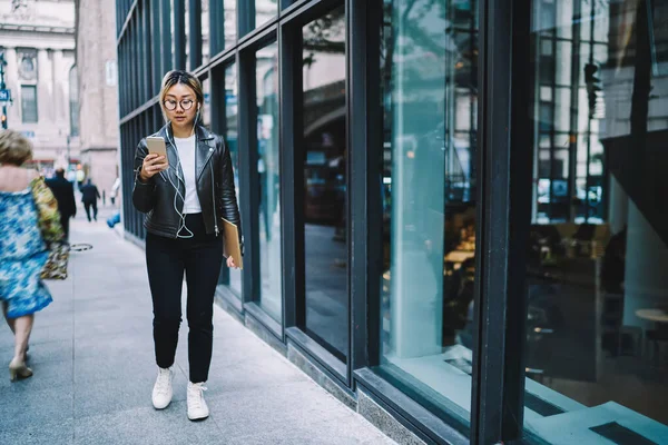 現代の携帯電話デバイス上のメディアアプリケーションを使用して 電子ヘッドフォンで日本の女性観光客 スケッチブックリスニング音楽と千年ヒップスター女の子は マルチメディアを閲覧するためのウェブサイトを選択します — ストック写真