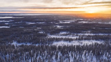 Laponya Ulusal Parkı 'ndaki bitmeyen kozalaklı ağaçların karlı çam ağaçlarından gelen hava manzarası kış mevsiminde gün batımında Riisitunturi' de kuş bakışı manzara.
