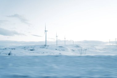 Norveç 'te karlı ve buzlu bir arazi. Soğuk kış havasında açık güneşli bulutlu gökyüzünün altında uzun yel değirmenleri var.