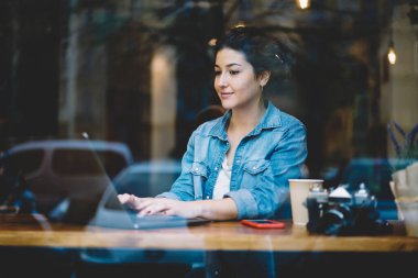 Modern dizüstü bilgisayarı olan düşünceli bir kadın kullanıcı kafeterya masasında oturmuş uzaktan kumandalı işi düşünüyor, netbook cihazlı düşünceli hippi kız web tasarımı fikri üzerinde kafa yoruyor.