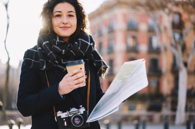 Güneşli sonbaharda seyahatlerin tadını çıkarmak için tek başına seyahat eden modaya uygun giyinmiş, geçmişe dönük kameralı beyaz kız portresi varış yerini arıyor.