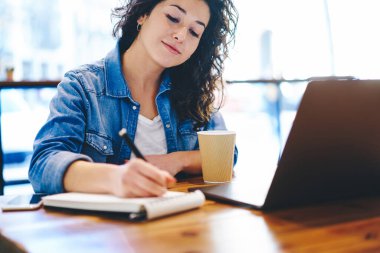 Eğitim notları yazan Millennial kız öğrenci kafeterya masasında modern laptopla eğitim için oturuyor. Akıllı hippi kız öğrenim süreci organizasyonu planlıyor.