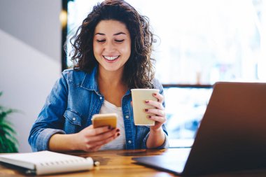 İnternette mesajlaşmak ve sohbet etmek için hücresel cihaz kullanmak için kahveyle gezen mutlu hippi kız, internet sitesini taramak için 4G 'ye bağlanan paket servis bardağıyla neşeli kadın blogcu