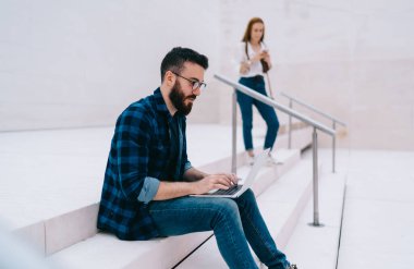 Gözlüklü bir erkek blogcu, modern dizüstü bilgisayarda 4G kablosuz, milenyum kullanıcısına bağlanan ve netbook okuma yoluyla uzaktan çalışan dergileri izlerken serbest internet projesi ile e-posta almış.