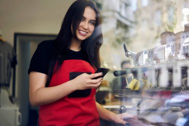 Önlüklü başarılı esmer kadın sanatçı kafeteryadaki işi bittikten sonra cep telefonu kullanıyor. 20 'li yaşlarda, elinde akıllı telefon paylaşımı içeriği olan akıllı telefon şirketinin kadın müdürü blogdaki işi hakkında gülümsüyor.