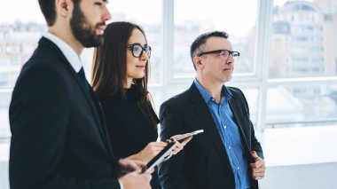 Group of Caucasian entrepreneurs discussing company briefing during working process in office interior, experienced male and female colleagues communicating about business and exchange marketing