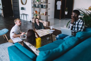 From above of cheerful multiracial people in casual clothes discussing route of trip in vacation together while gathering in contemporary apartment