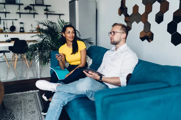 Jóvenes Amigos Multiétnicos Ropa Casual Sentados Sofá Apartamento Moderno Hablando —  Fotos de Stock