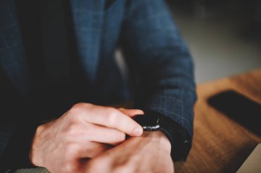 Cropped male manager using wearable digital smartwatch for checking time during working day in office, unrecognizable businessman touching screen of modern wrist clock looking on display indoors