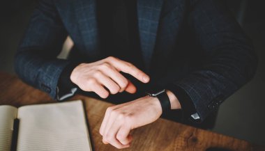 Cropped male manager using wearable digital smartwatch for checking time during working day in office, unrecognizable businessman touching screen of modern wrist clock looking on display indoors