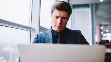 Serious male businessman in formal wear watching informative video and reading web news via multimedia application on modern laptop device,Caucasian male entrepreneur making online booking and banking