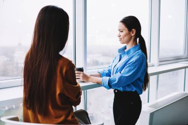 Female employee talking with executive manager discussing idea during coffee break in interior office, Caucaisan colleagues with disposable takeaway cup communicating about business project
