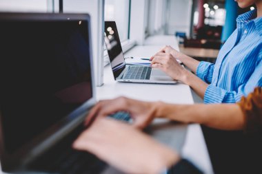 Cropped female coworkers using laptop computers for sharing media content during remote brainstorming working, bloggers searching website for browsing wireless publication and watching video
