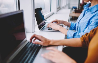 Unrecognizable women sharing media files using bluetooth connection on modern netbooks, cropped view of skilled IT professionals programming and typing software text via laptop application