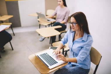 High angle of young concentrated female company employee typing on laptop while meeting with colleagues in small conference room in office