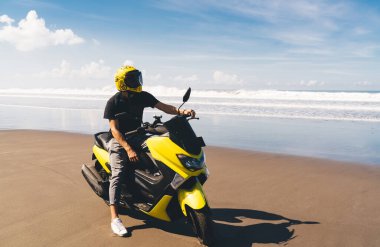 Unrecognizable biker in casual wear and helmet with stylish motorbike enjoying freedom while riding at seaside on sunny summer day