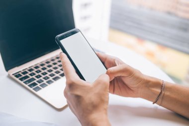 Güneşli bir günde kafede dizüstü bilgisayar başında çalışırken boş ekranlı akıllı telefon kullanan yüzü olmayan kadın serbest yazar yüksek açılı.