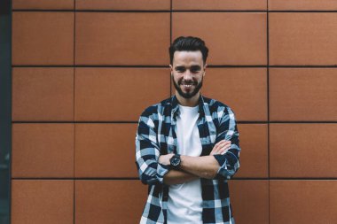 Şık sokak kıyafetleri giymiş neşeli hippi adam şehrin reklam bölgesinde poz veriyor.