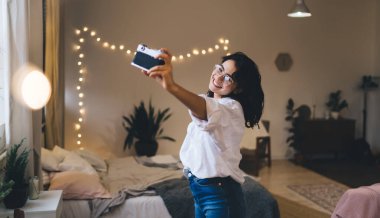 Saçları dökülmüş, eski moda fotoğraf makinesiyle rahat bir odada duvarda parlayan ışıklarla kendi portresini çeken hoş bir kadın.